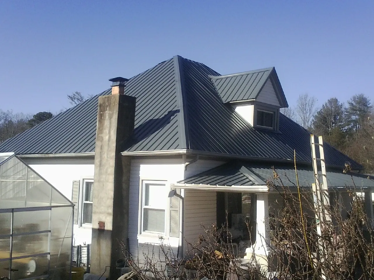 Dark blue standing seam metal roof on a white farmhouse with dormer — Slate & Tile Roof Repair by Roofing Brothers in Grainfield