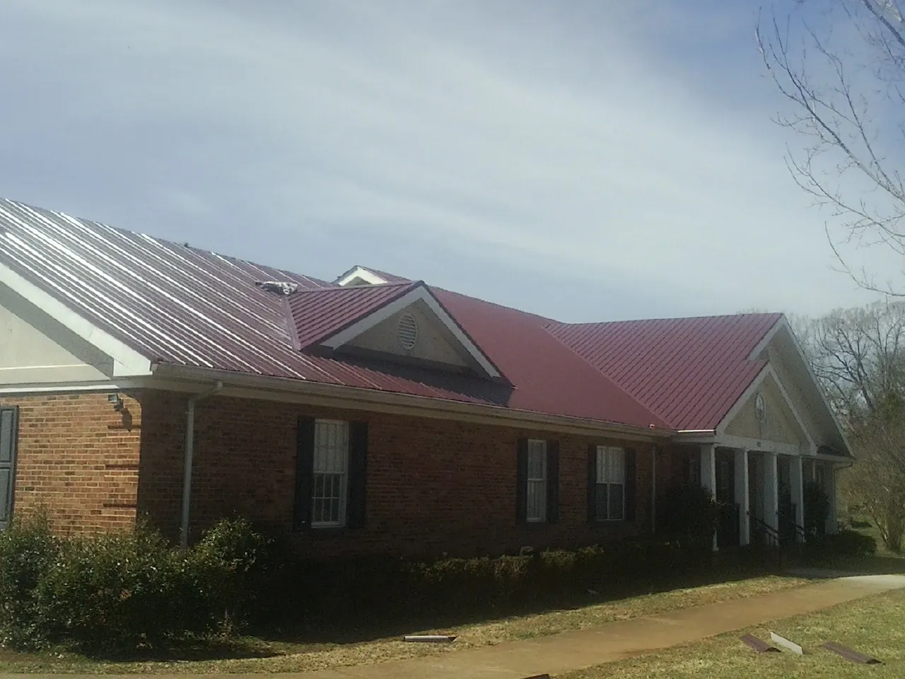 Red metal roof with gabled entries on a long brick building, from a Hail Damage Roof Repair job in Grainfield