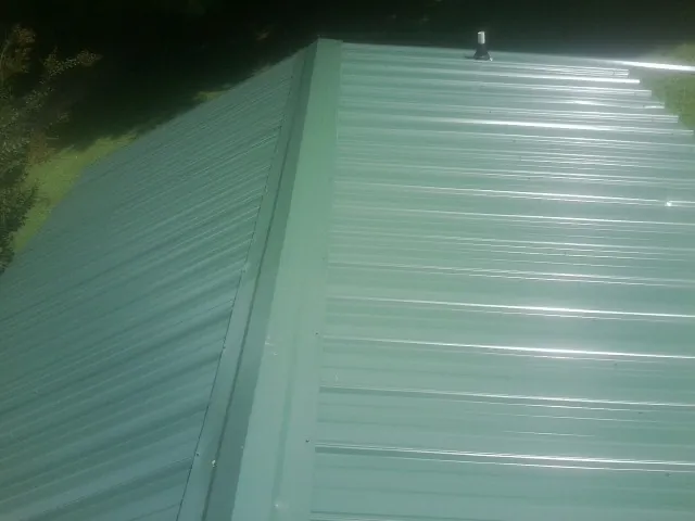 New green metal panels meeting at the ridge of a roof — Flat Roof Repair work by our crew in Grainfield