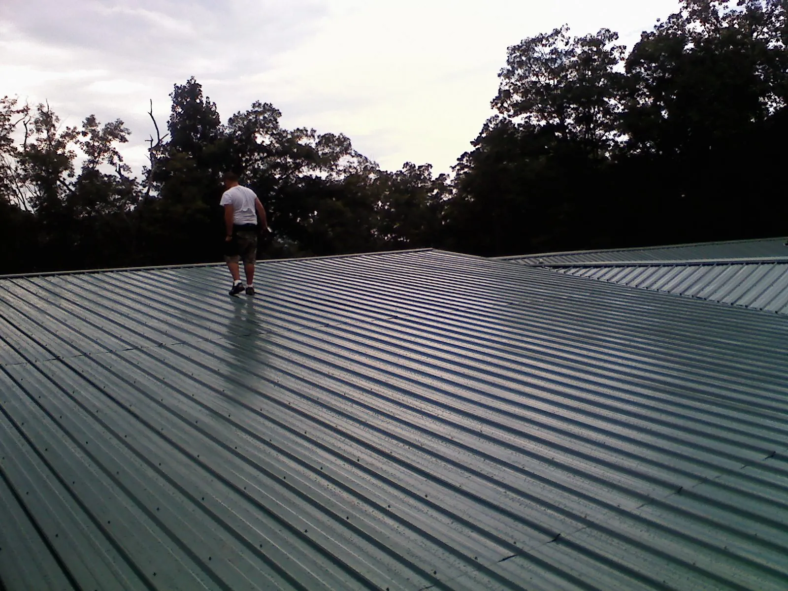 Roofer walking a wide expanse of new green metal roofing in Grainfield