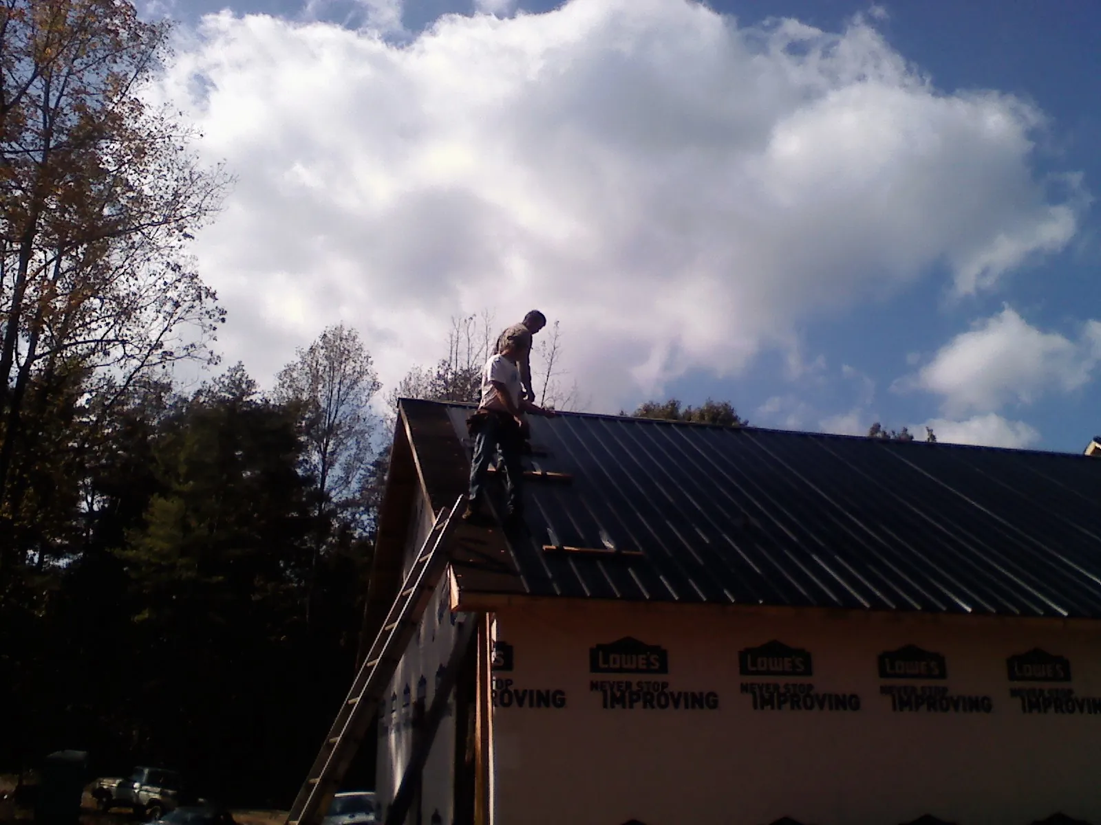 Roofer fastening dark metal panels high against a cloudy sky, from a Roof Inspection job in Grainfield