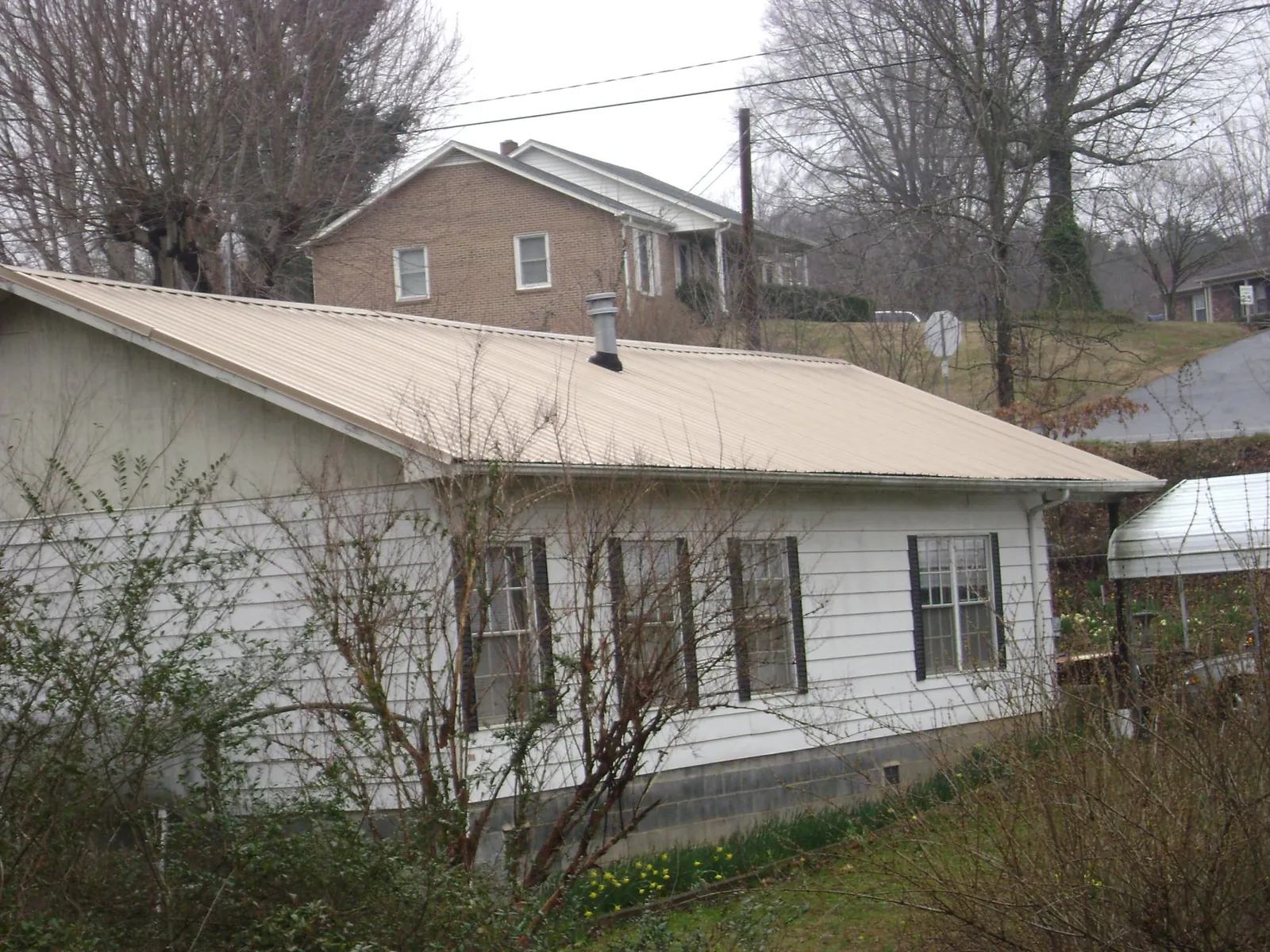 Tan metal roof on a white sided house set into a hillside — Commercial Roofing by Roofing Brothers in Grainfield