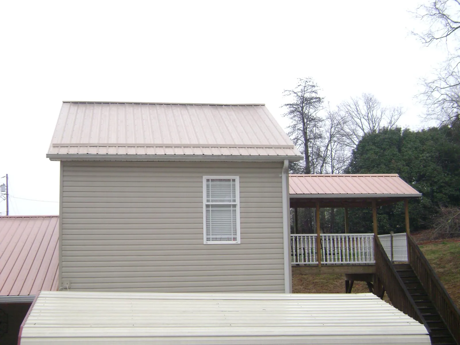 Tan metal roofs on a two story addition and attached porch, from a Roof Replacement job in Grainfield