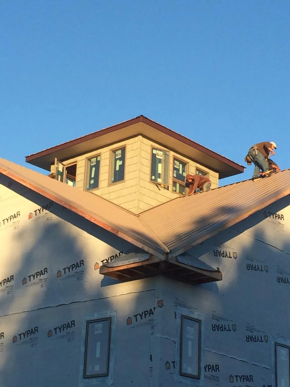 Roofers working around a rooftop cupola on a new metal roof at sunset — Roof Waterproofing in Grainfield by Roofing Brothers